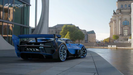 HD PC desktop wallpaper from the video game Gran Turismo Sport featuring a detailed blue sports car parked in an urban setting with modern and historic architecture.