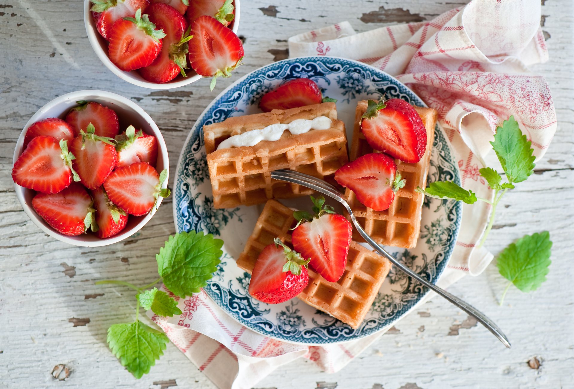 Still life breakfast: waffles with cream, sliced strawberries and mint on a decorative plate, bowls of berries — 4K Ultra HD PC desktop wallpaper.
