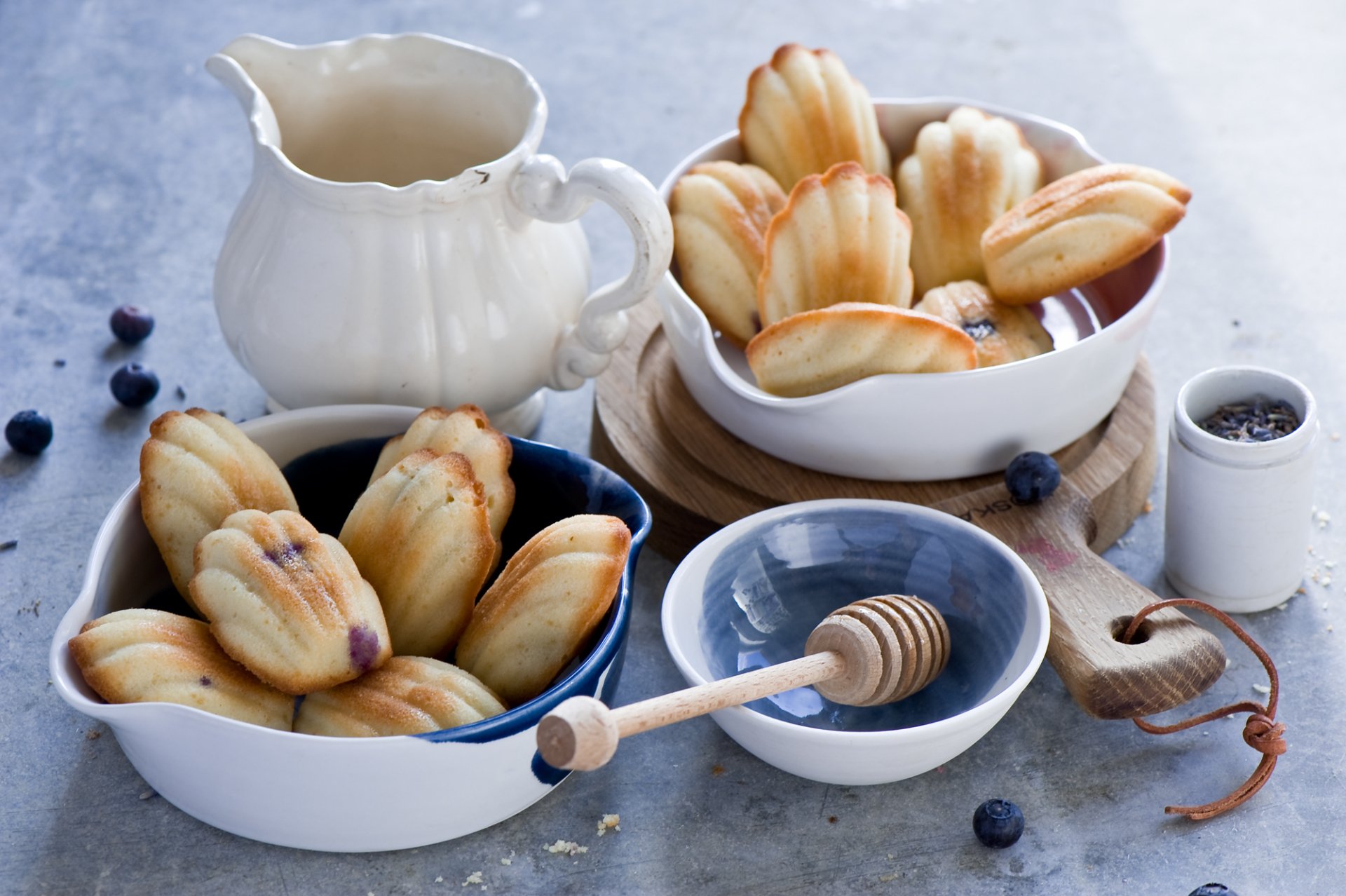 HD PC desktop wallpaper/background: still life food scene of madeleines in white bowls with honey dipper, milk jug and scattered blueberries.