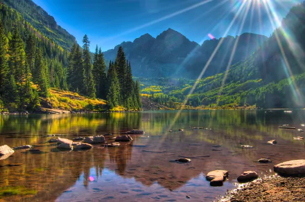 4K Ultra HD desktop wallpaper showcasing the serene Maroon Bells mountains with clear lake reflections, vibrant greenery, and sunlight streaming through a bright blue sky.