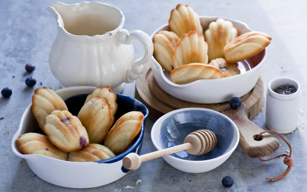 HD PC desktop wallpaper/background: still life food scene of madeleines in white bowls with honey dipper, milk jug and scattered blueberries.
