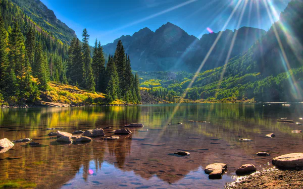 4K Ultra HD desktop wallpaper showcasing the serene Maroon Bells mountains with clear lake reflections, vibrant greenery, and sunlight streaming through a bright blue sky.