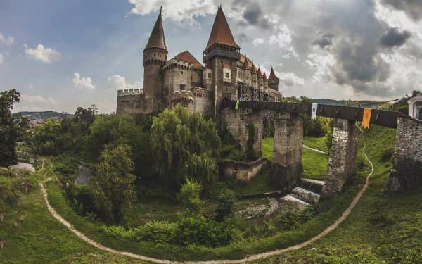 A majestic man-made castle in Hungary with tall towers, a stone bridge, and lush greenery, captured in stunning 4K Ultra HD for a PC desktop wallpaper.
