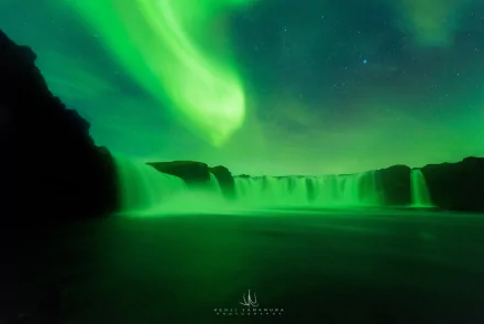 A captivating view of the Goðafoss waterfall illuminated by a stunning green aurora borealis in Iceland, showcasing the beauty of nature under a starry night sky.