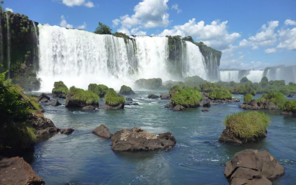 A stunning 4K Ultra HD image of Iguazu Falls showcasing cascading waterfalls surrounded by lush greenery and flowing river under a bright blue sky.