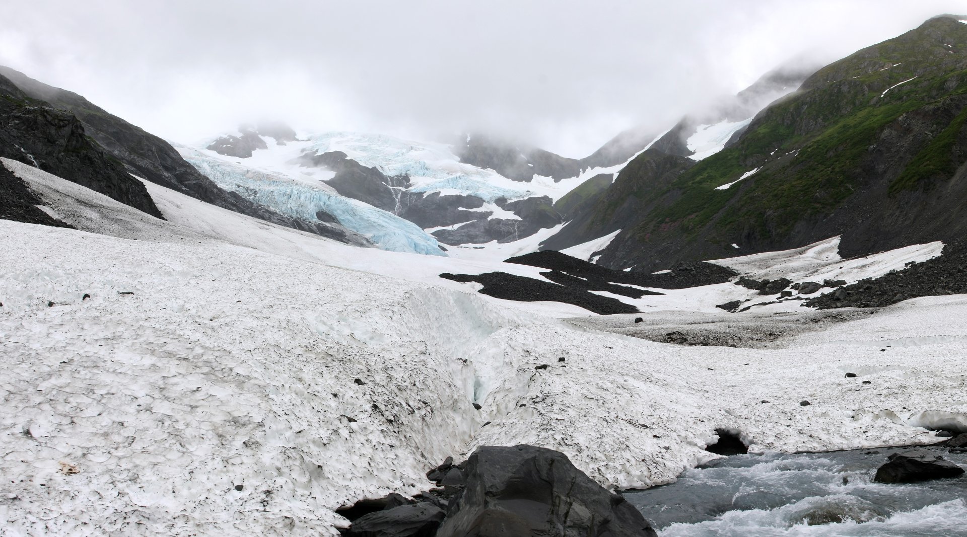 4K Ultra HD PC desktop wallpaper showing a nature scene: panoramic glacier valley with blue ice flows, snowfields, rocky foreground and misty cloud-covered peaks.