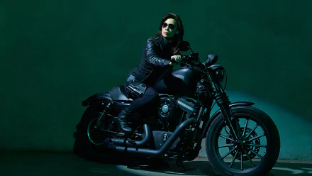 HD desktop wallpaper featuring a character from the TV show Agents of S.H.I.E.L.D. sitting confidently on a black motorcycle against a dark green background.