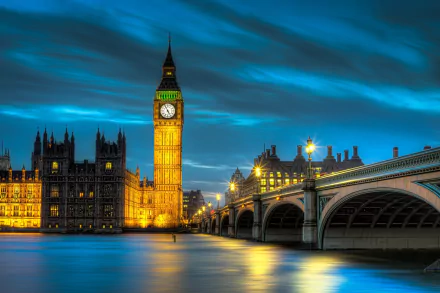 A stunning night view of the Palace of Westminster and Big Ben illuminated against a dynamic blue sky, reflecting beautifully on the River Thames in London. A captivating HD wallpaper.