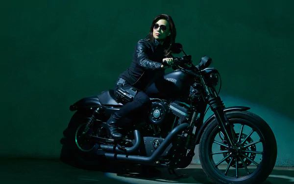 HD desktop wallpaper featuring a character from the TV show Agents of S.H.I.E.L.D. sitting confidently on a black motorcycle against a dark green background.