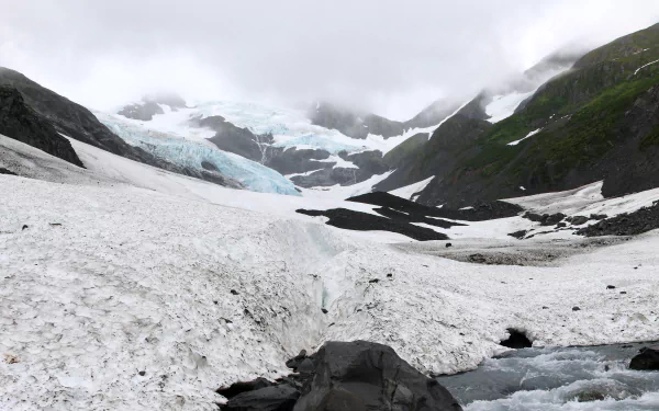 4K Ultra HD PC desktop wallpaper showing a nature scene: panoramic glacier valley with blue ice flows, snowfields, rocky foreground and misty cloud-covered peaks.