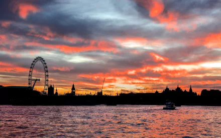 Silhouetted London skyline with the man-made London Eye ferris wheel by the Thames beneath a cloud-streaked sunset sky — HD England city desktop wallpaper.