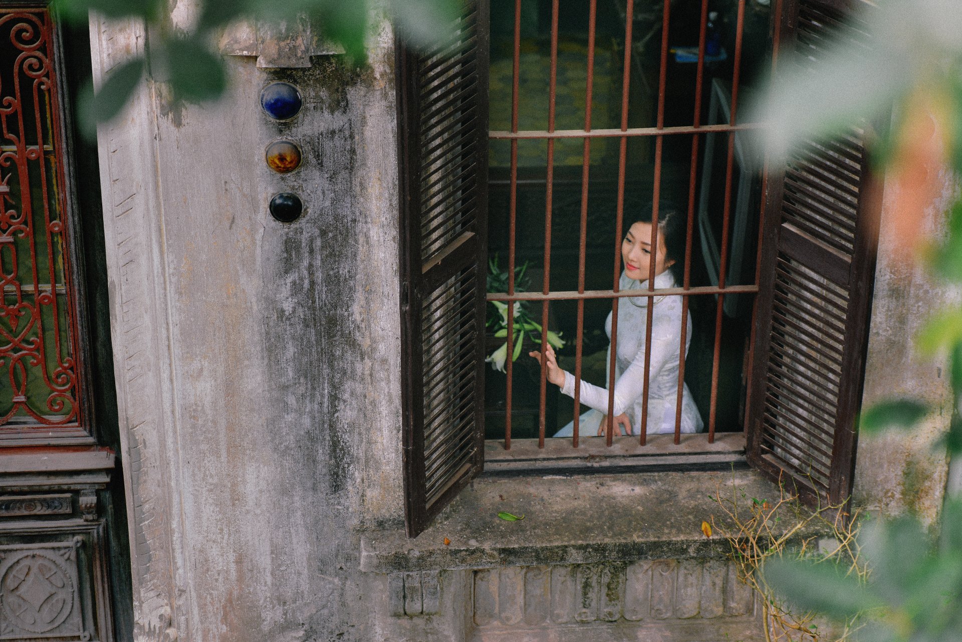 A Vietnamese woman in a traditional white Ao Dai stands behind wooden window bars, captured in a serene 4K Ultra HD desktop wallpaper setting.