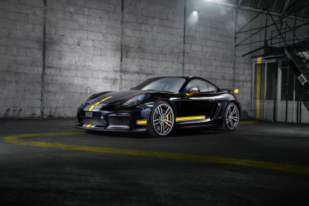 Black Porsche Cayman GT4 with yellow racing stripes parked in an industrial setting, featured as an HD PC desktop wallpaper and background.