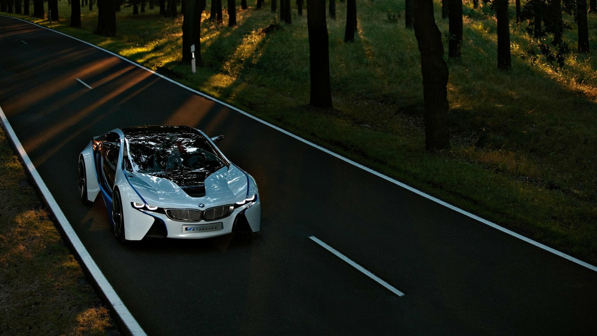 A sleek BMW i8 drives along a winding road, surrounded by trees, creating a striking HD PC desktop wallpaper and background. The vibrant contrast highlights the car's futuristic design.