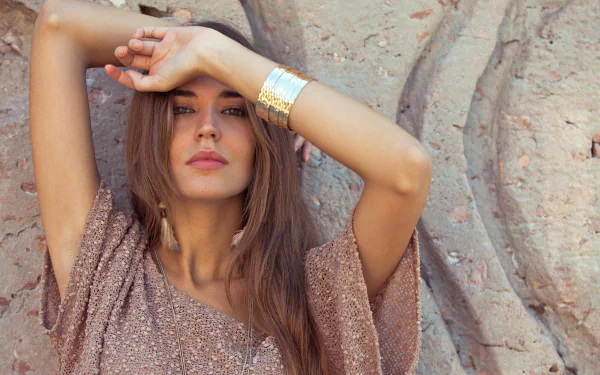 4K Ultra HD portrait of Spanish woman Clara Alonso posing against a textured stone background, wearing a shimmering top and a gold cuff bracelet.