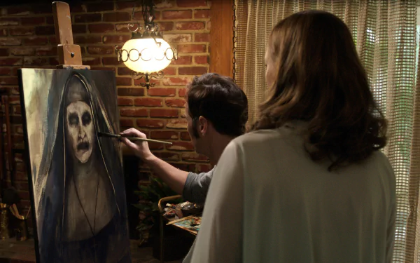 A scene from *The Conjuring 2* shows a man painting a haunting portrait of a nun, while a woman observes. The rustic setting enhances the eerie atmosphere of the film.