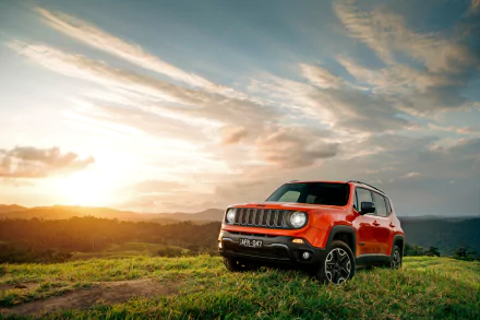 Orange Jeep Renegade SUV parked on grassy terrain at sunset under a dramatic sky, captured in 4K Ultra HD for a PC desktop wallpaper background.