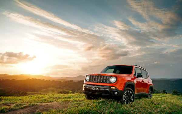 Orange Jeep Renegade SUV parked on grassy terrain at sunset under a dramatic sky, captured in 4K Ultra HD for a PC desktop wallpaper background.