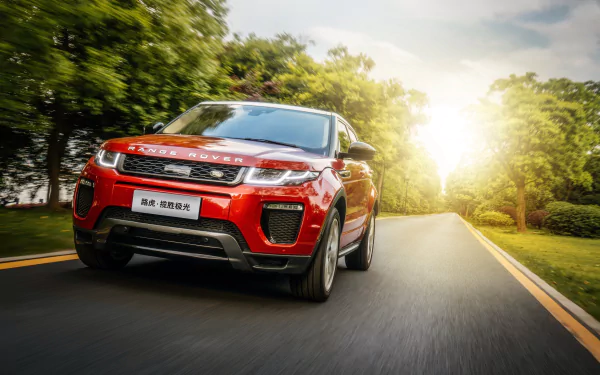 A dynamic view of a red Range Rover Evoque SUV driving along a scenic road, surrounded by lush greenery and illuminated by natural sunlight. 4K Ultra HD wallpaper.