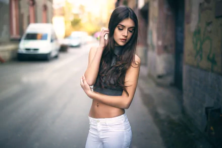 HD desktop wallpaper of a brunette woman model wearing white jeans, posing thoughtfully on a blurred urban street background.