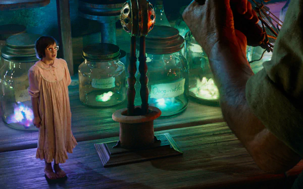 A scene from the movie The BFG (2016), featuring a young girl in a flowing dress standing beside a giant, surrounded by glowing jars in a whimsical, colorful setting.