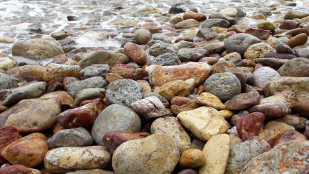 Close-up of multicolored shoreline stones with lapping surf — a nature scene presented as a 2K Quad HD PC desktop wallpaper/background.