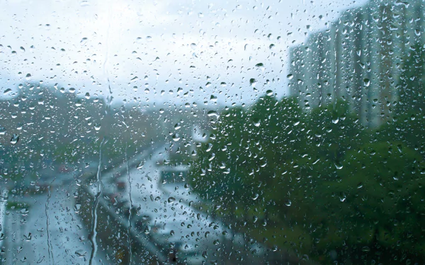 A close-up view of raindrops on a window, creating a blurred effect, with a rainy cityscape visible in the background, making it a captivating HD wallpaper.
