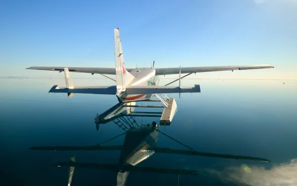 A Cessna seaplane floats on calm water, its reflection mirrored perfectly beneath clear blue skies in a 4K Ultra HD desktop wallpaper.