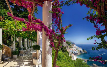 A stunning view of Amalfi, Italy, framed by vibrant flowers and greenery. Man-made structures blend harmoniously with the natural beauty of the landscape and coastal scenery.