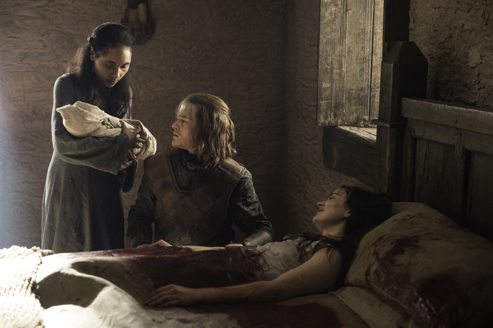 Game of Thrones TV 2K Quad HD desktop wallpaper: dim Stark bedside scene — a woman cradling a newborn, a man seated watching, another person lying on the bed.