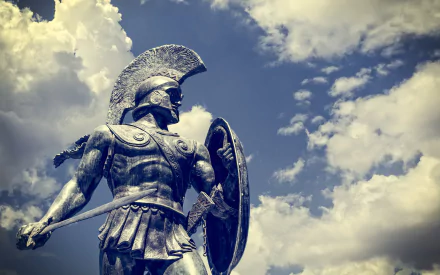 A majestic statue of a Greek warrior stands against a dramatic sky, capturing the essence of history and valor, serving as a striking HD desktop wallpaper and background.