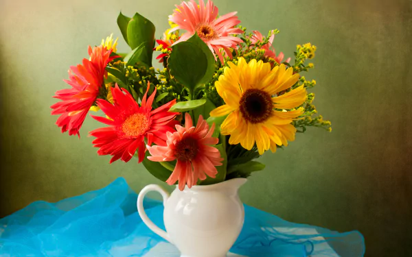 Colorful still-life of red, pink and yellow gerbera bouquet in a man-made white vase on blue cloth — vibrant 8K Ultra HD PC desktop wallpaper background.
