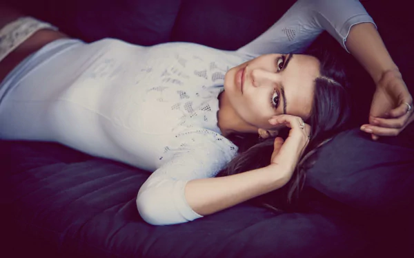 A brunette model with brown eyes relaxes elegantly on a dark surface, showcasing her style and poise, set against a soft-focus background for a striking HD wallpaper.