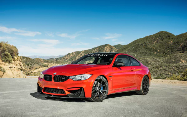 HD desktop wallpaper featuring a red BMW M4 grand tourer parked on a mountain road with clear blue skies and rugged hills in the background.