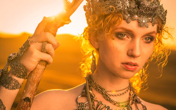 Close-up of redhead model Alexandria Basso with green eyes, wearing an ornate necklace and headpiece, bathed in warm sunny light, HD desktop wallpaper background.