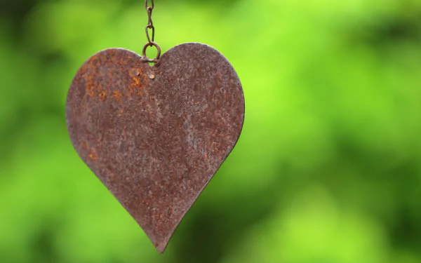 Artistic HD PC desktop wallpaper: a rusted metal heart pendant on a chain against a soft green blurred background.