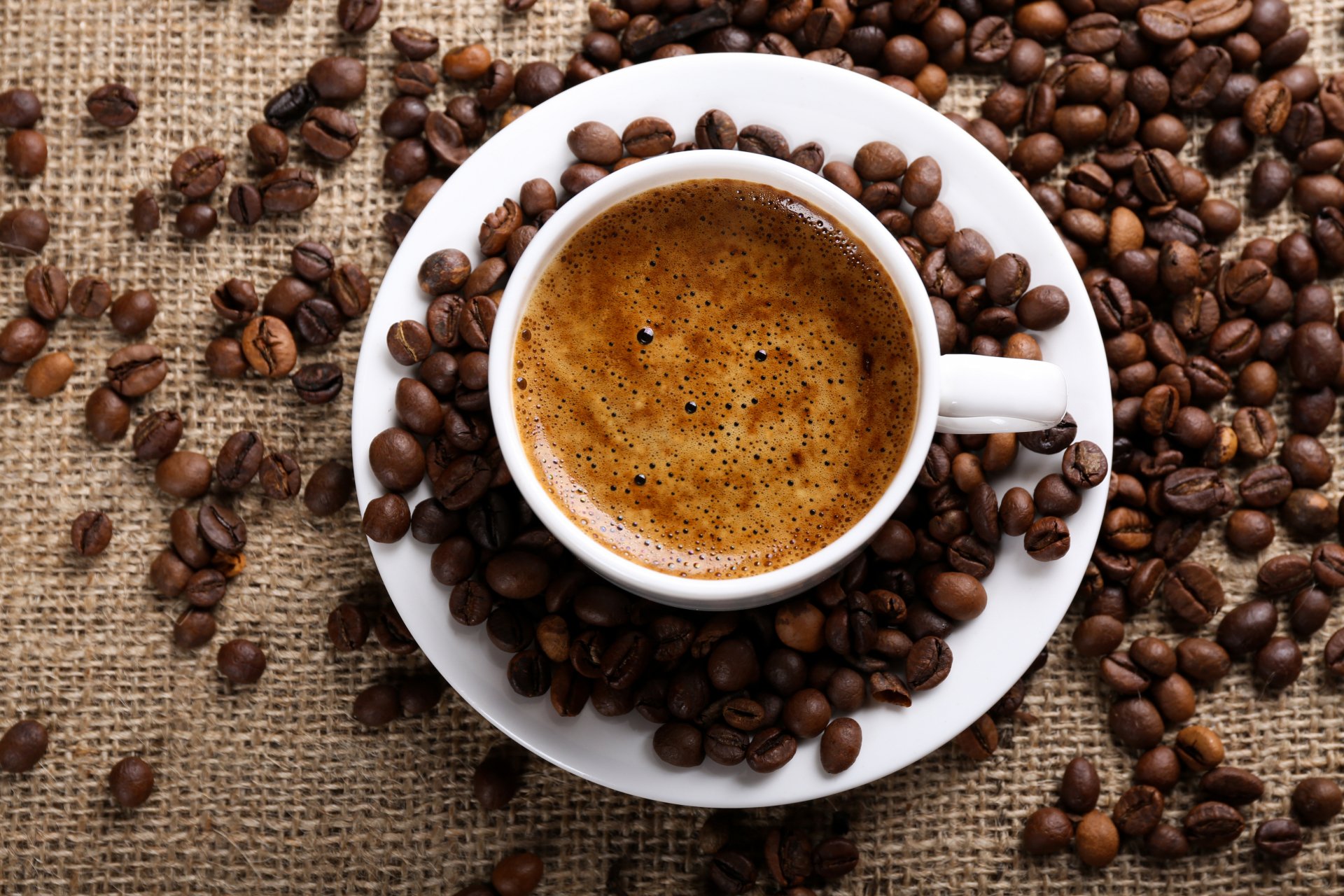 5K Ultra HD PC desktop wallpaper: top view of a steaming cup of coffee on a saucer surrounded by roasted coffee beans on burlap.