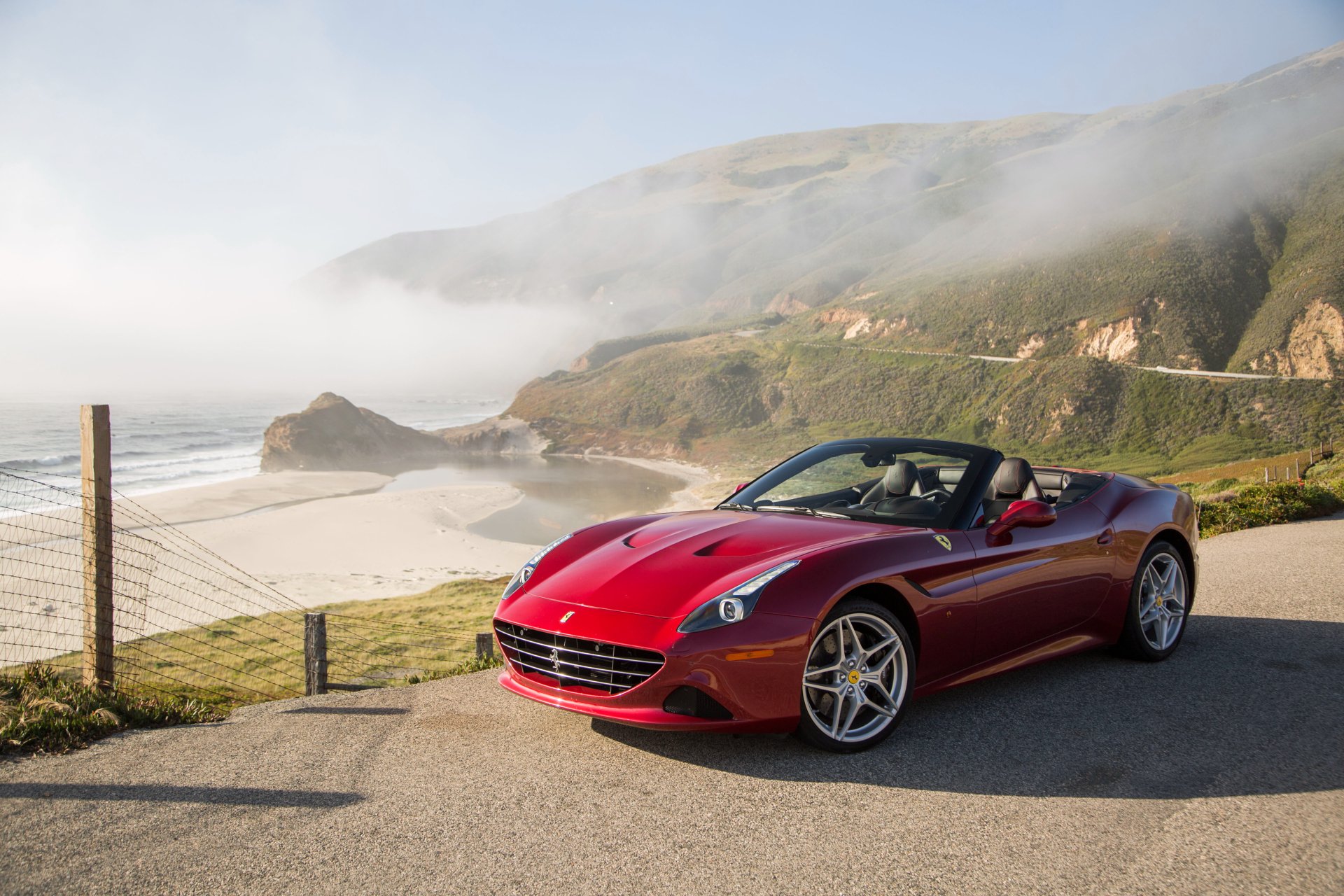 Red Ferrari California grand tourer car parked on a coastal road with cliffs and ocean mist — 4K Ultra HD PC desktop wallpaper background.