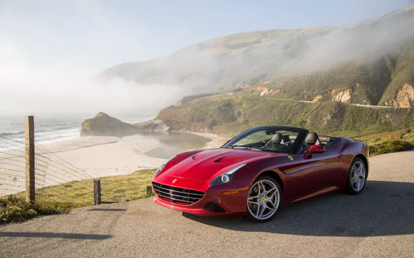 Red Ferrari California grand tourer car parked on a coastal road with cliffs and ocean mist — 4K Ultra HD PC desktop wallpaper background.