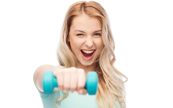 A smiling blonde woman in a fitness outfit holds a blue dumbbell, exuding energy and enthusiasm. This 4K Ultra HD wallpaper captures her sporty spirit.