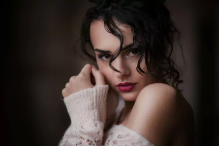 HD desktop wallpaper featuring a brunette model with brown eyes and lipstick, gazing at the camera with a soft expression. She is wearing a light-colored sweater, adding a cozy feel to the image.