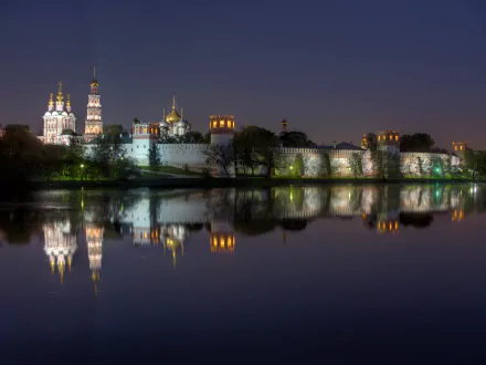 Night view of Novodevichy Convent in Moscow, Russia, with illuminated religious monastery buildings reflecting on the calm river in a 4K Ultra HD wallpaper.