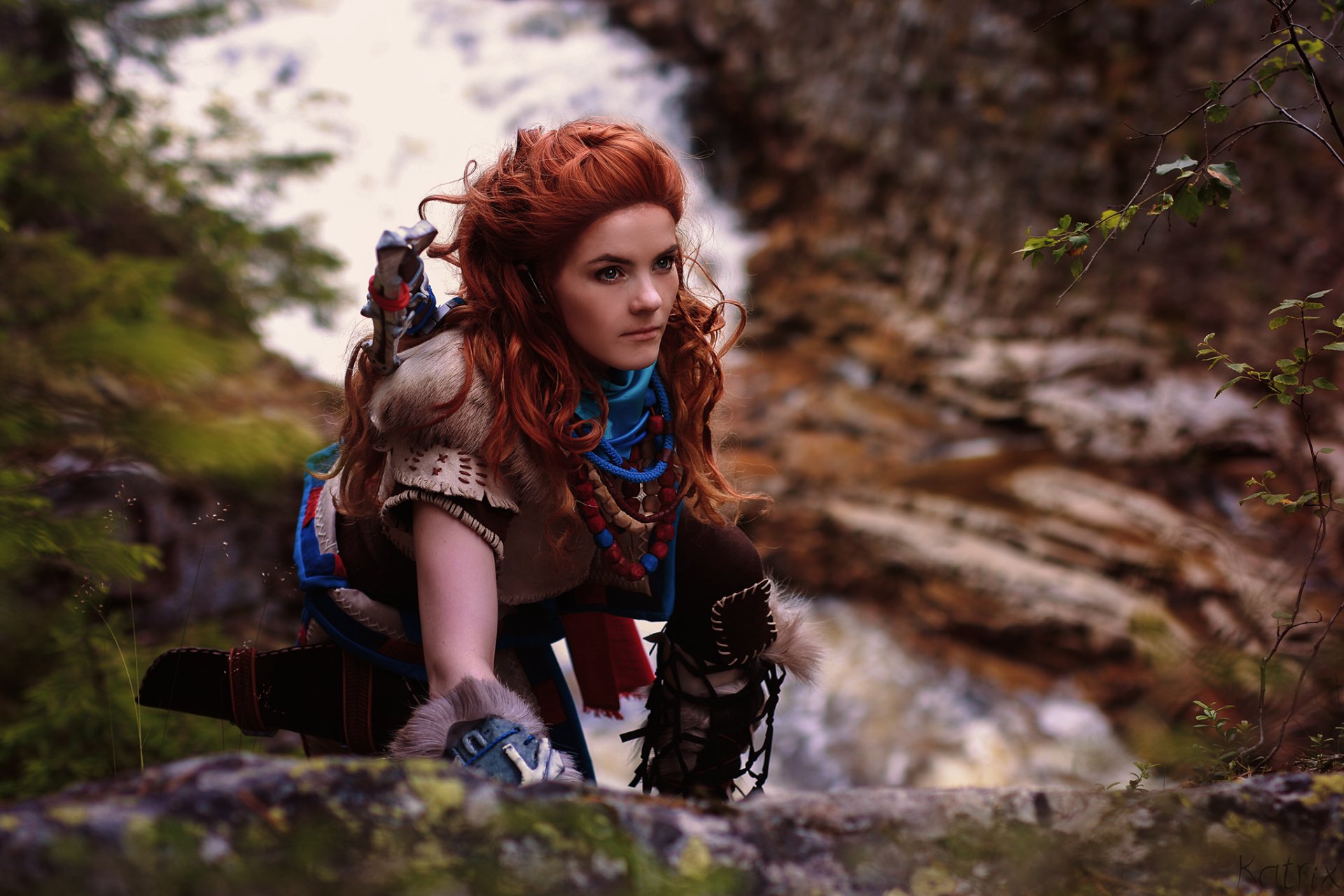 A vibrant HD wallpaper featuring a woman with red hair cosplaying as Aloy from the Horizon series, set against a natural landscape that evokes the world of Horizon Zero Dawn.