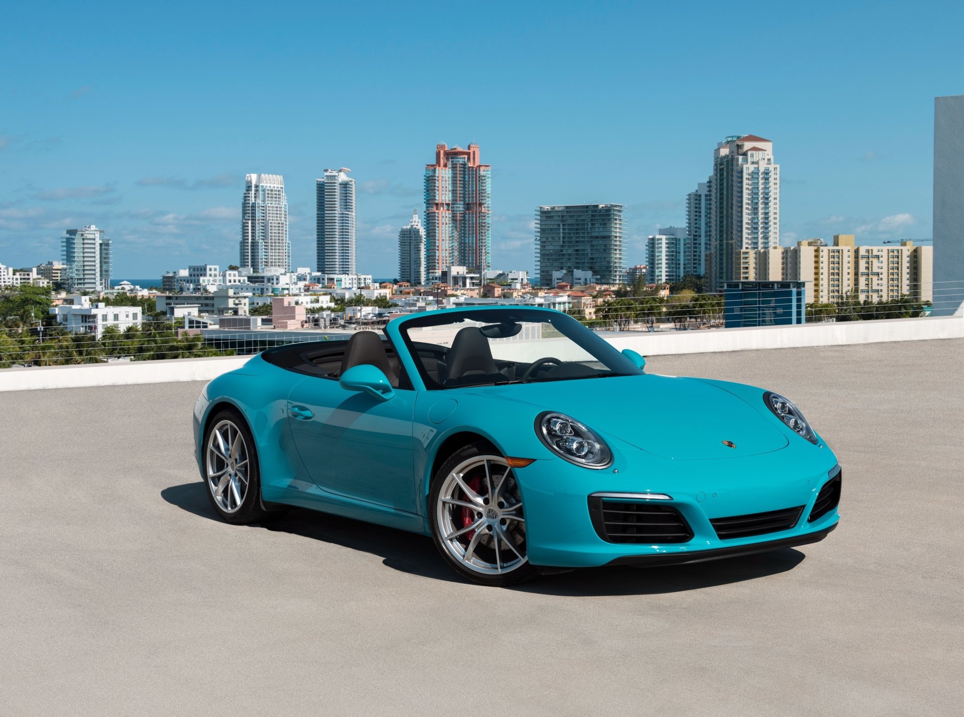 A turquoise Porsche 911 Carrera convertible parked on a rooftop with a city skyline in the background, captured in stunning 4K Ultra HD quality.