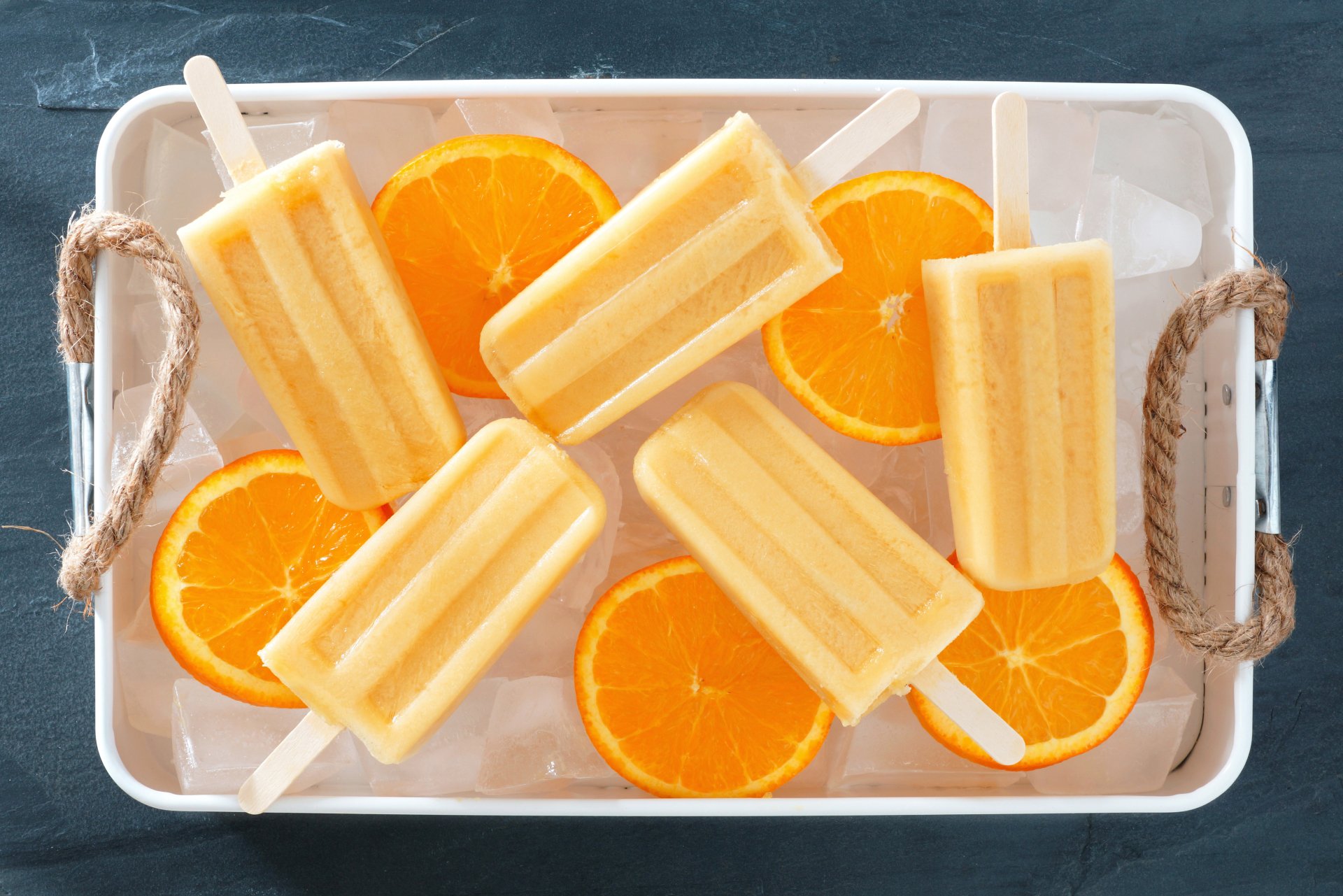 4K Ultra HD wallpaper featuring orange ice cream popsicles and ice cubes arranged on a tray with fresh orange slices, showcasing vibrant food textures.