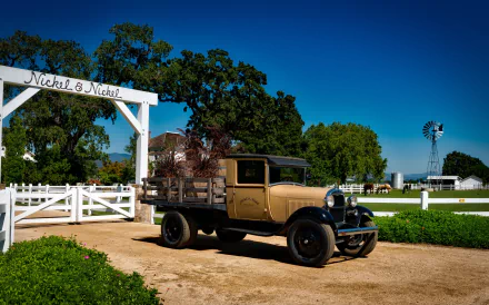 Vintage truck parked on a dirt path near a white gate labeled Nickel & Nickel, surrounded by greenery and a windmill under a clear blue sky in this HD desktop wallpaper.