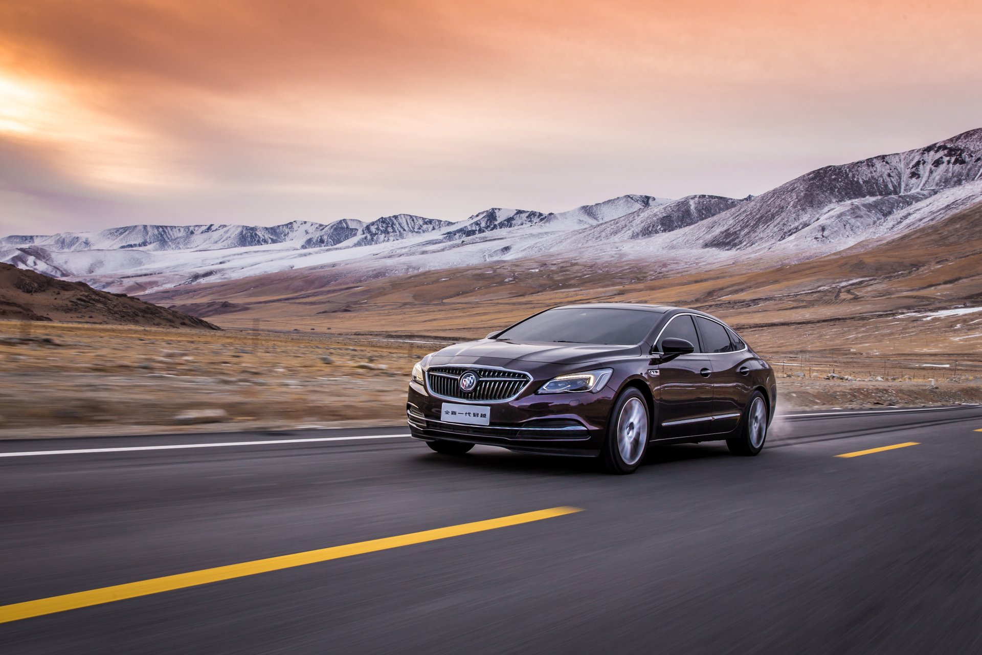 Sleek black Buick LaCrosse driving on an open road with mountainous landscape under a vibrant sunset sky, captured in 4K Ultra HD for PC desktop wallpaper.