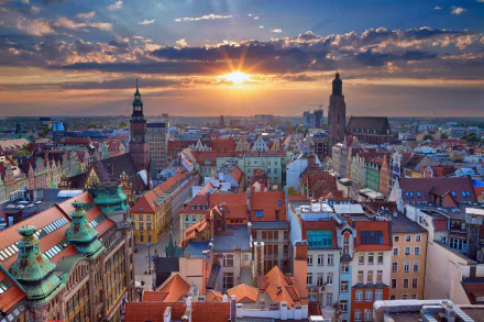 Panoramic sunset cityscape of Wrocław, Poland, horizon glowing over historic rooftops and church spires — vibrant HD PC desktop wallpaper background of a man-made urban panorama.