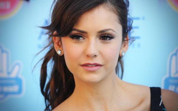 Nina Dobrev, a Canadian actress with brown eyes and brunette hair, poses elegantly against a vibrant blue background, captured in this HD desktop wallpaper.