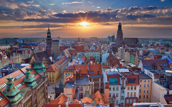 Panoramic sunset cityscape of Wrocław, Poland, horizon glowing over historic rooftops and church spires — vibrant HD PC desktop wallpaper background of a man-made urban panorama.